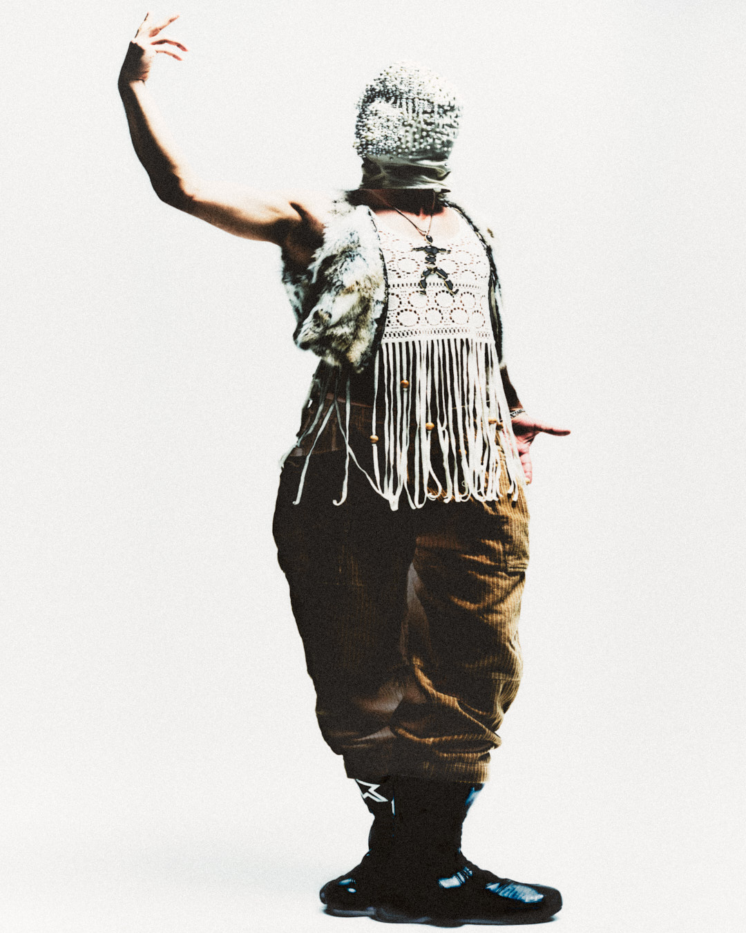 male model with one hand high facing the camera dressed in mask fur and corduroy pants