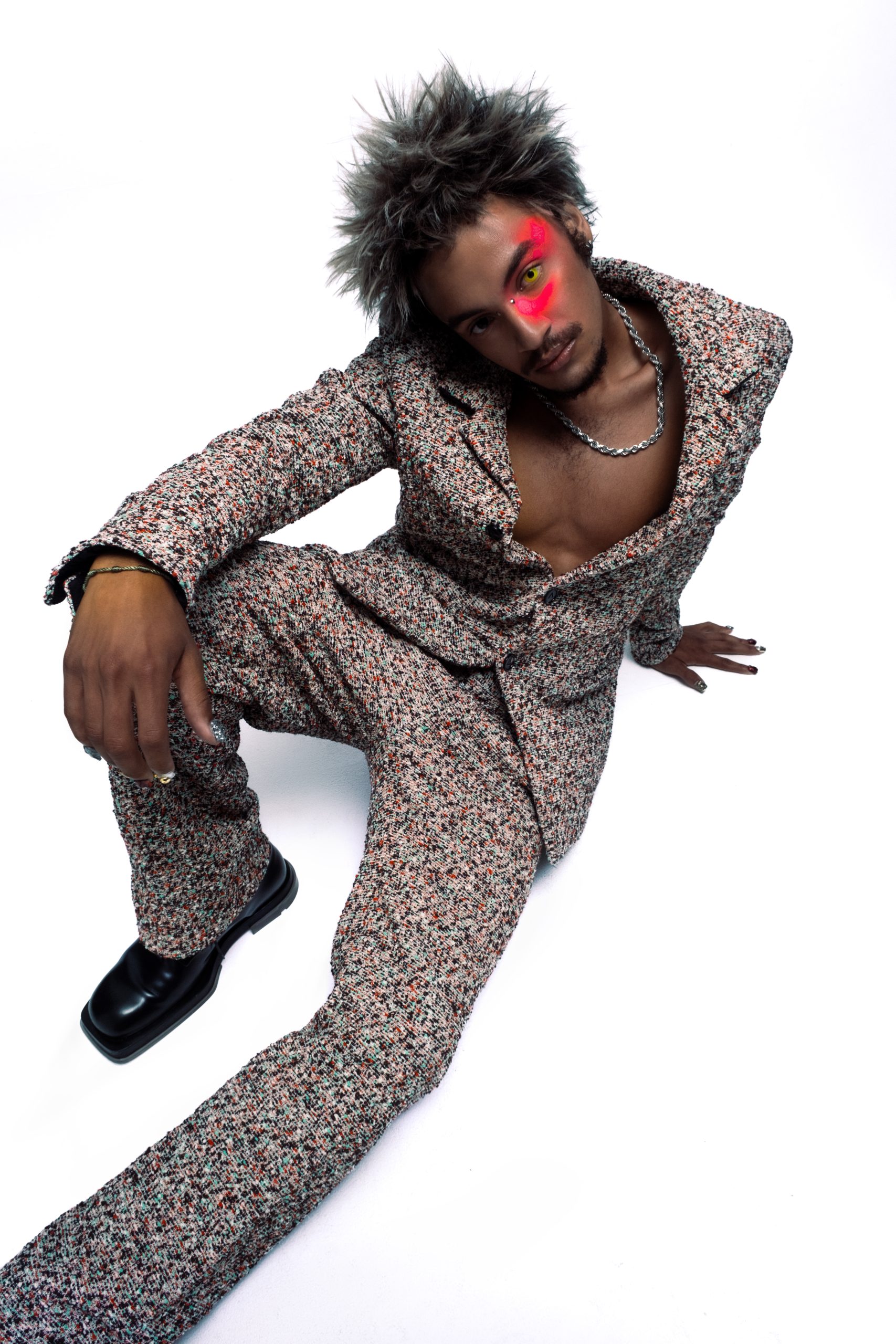 wide angle shot of balck model in dotted colorful suit and neon makeup sitting on the ground