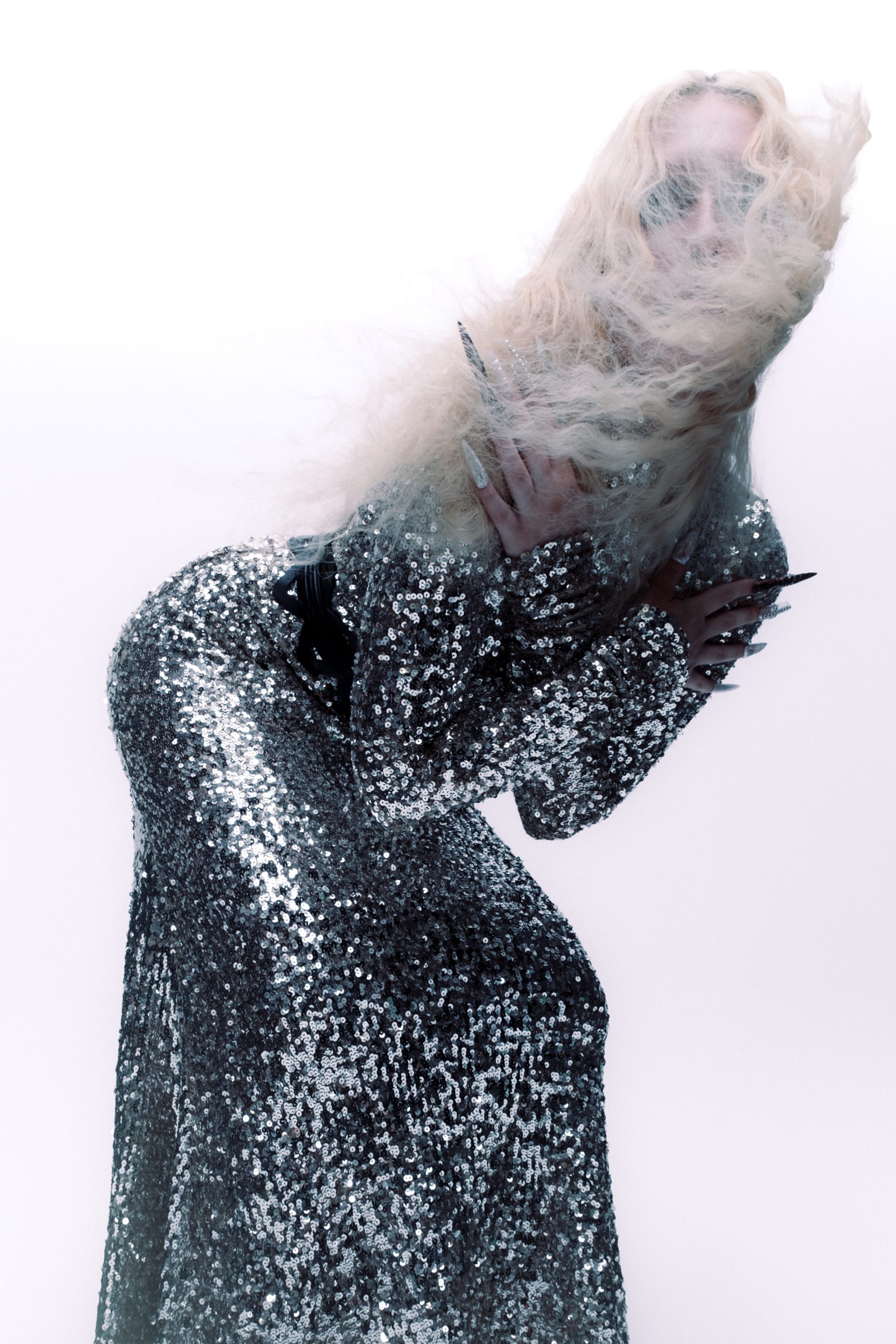 Three Quarter shot of model bending down to the side with hair her hair blowing into hair face dressed in sequin dress and long nails