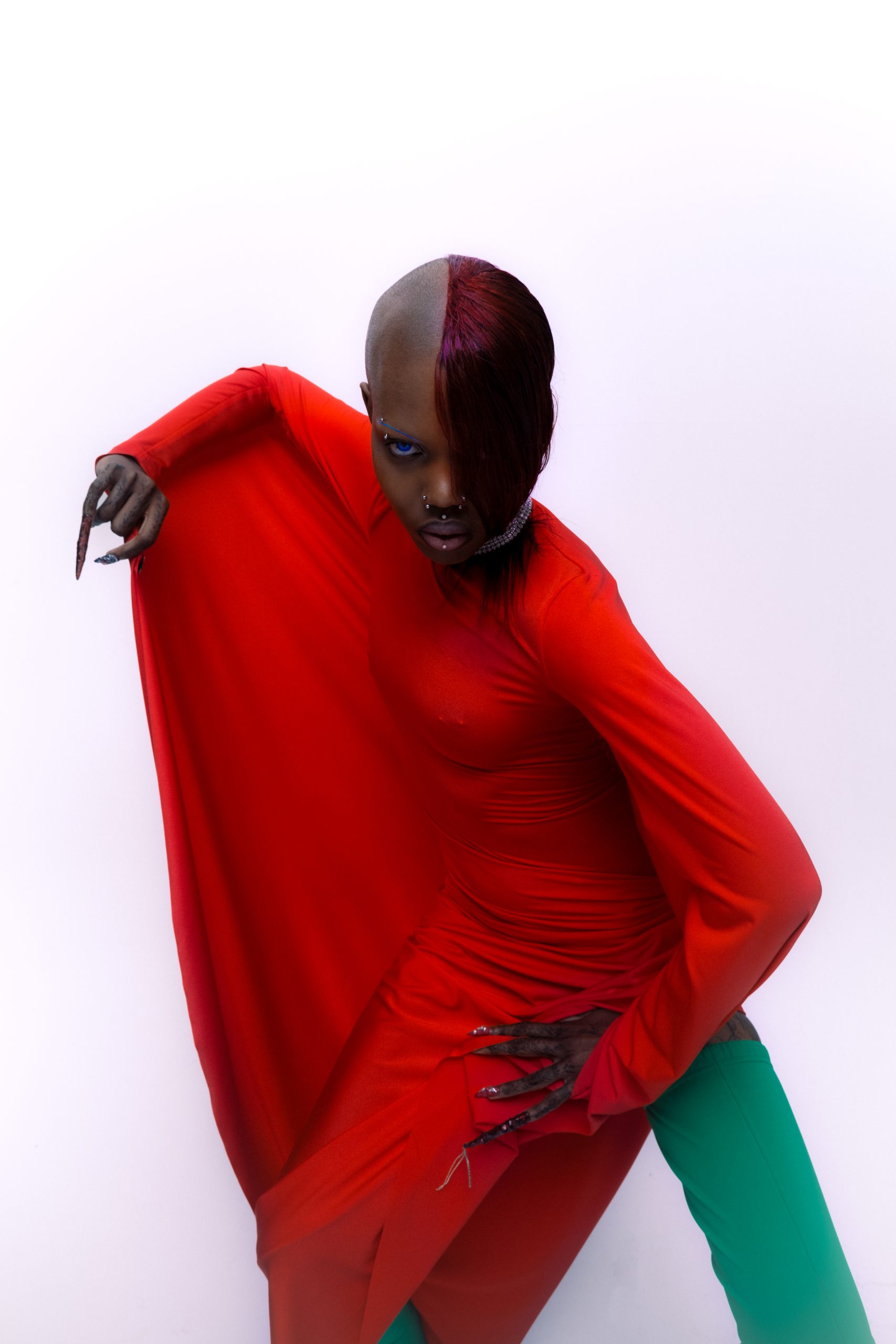 three quarter shot of black model looking into the camera with open mouth holding her face dressed in red