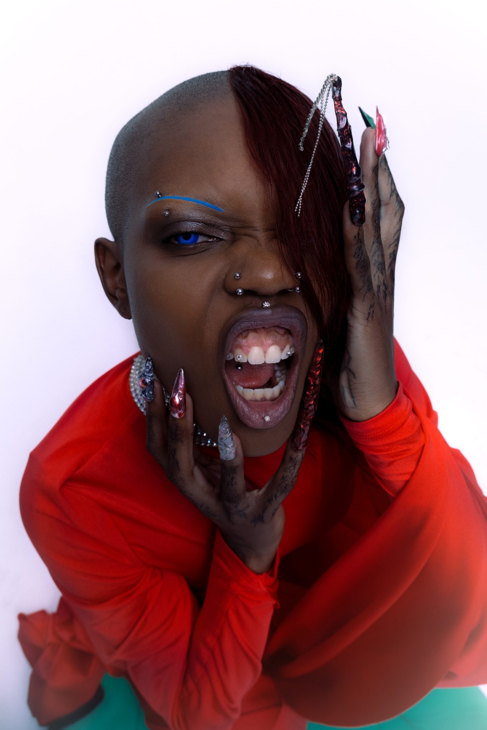 Closeup shot of black model looking into the camera with open mouth holding her face dressed in red