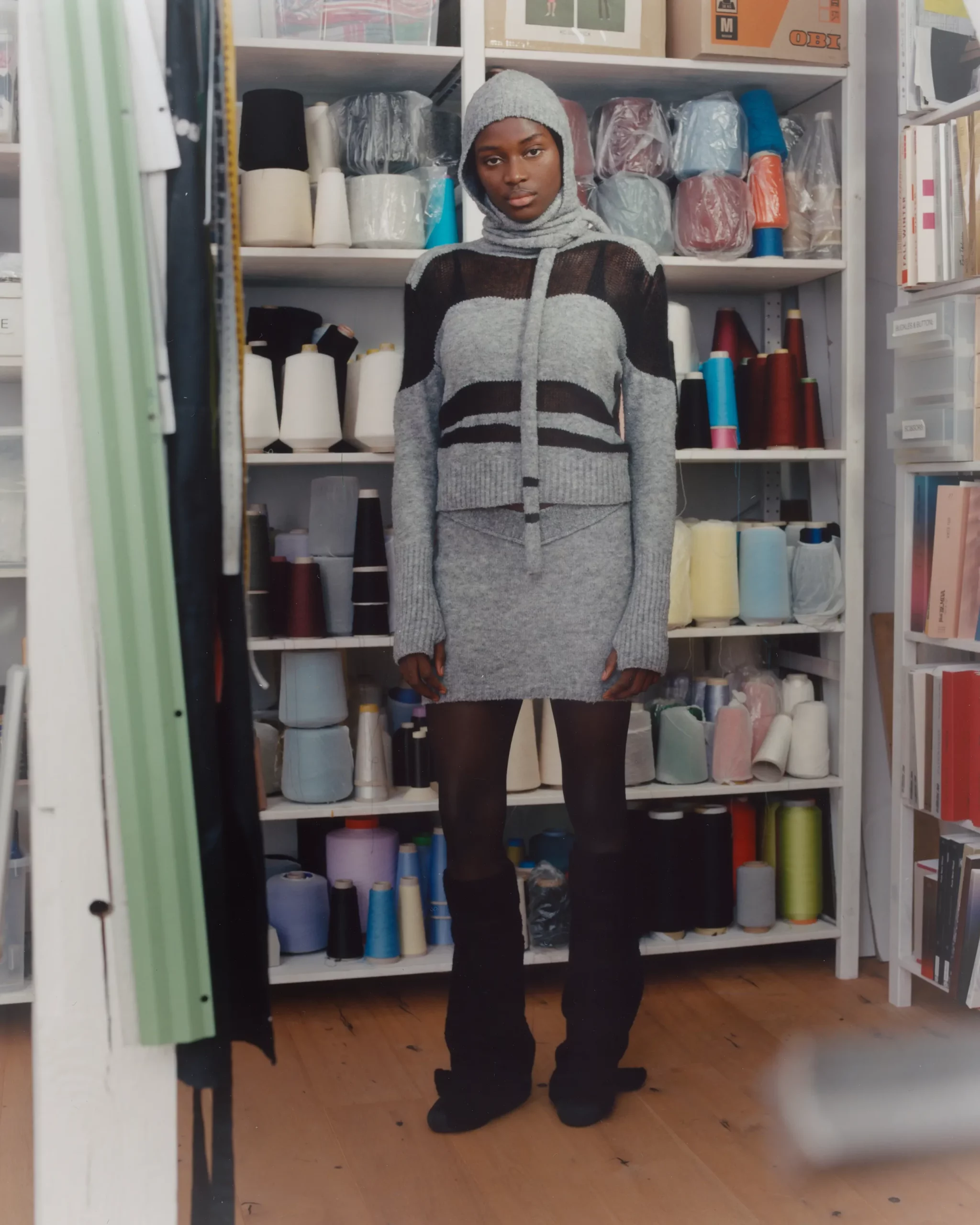 Female black model Ibukun Sammy wearing a design including a hat by Berlin based knitwear designer Katharina Dubbick in the designer's studio. Photographed by Charlotte Helwig.