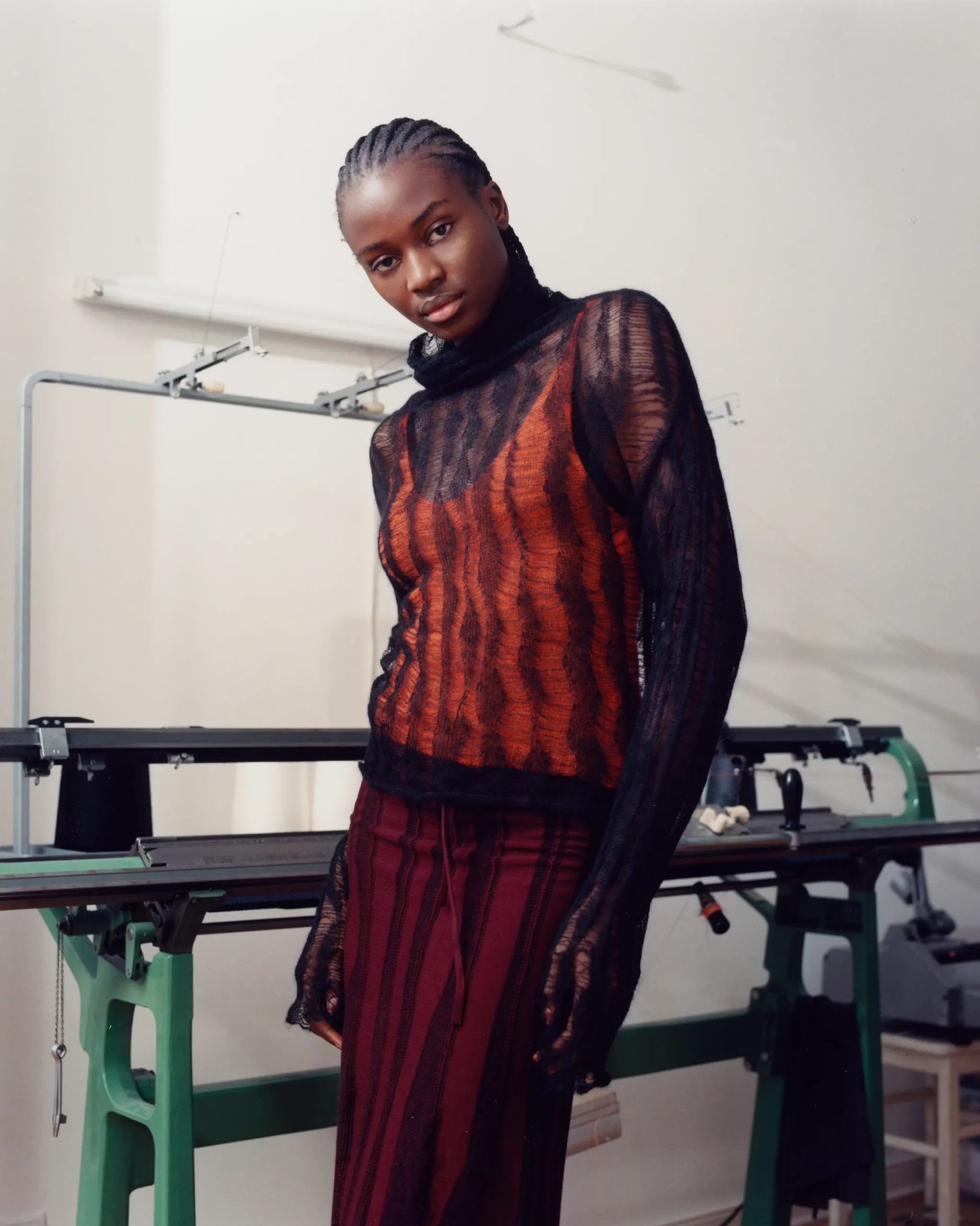 Female black model Ibukun Sammy wearing a design by Berlin based knitwear designer Katharina Dubbick in the designer's studio in front of a knitting machine. Photographed by Charlotte Helwig.