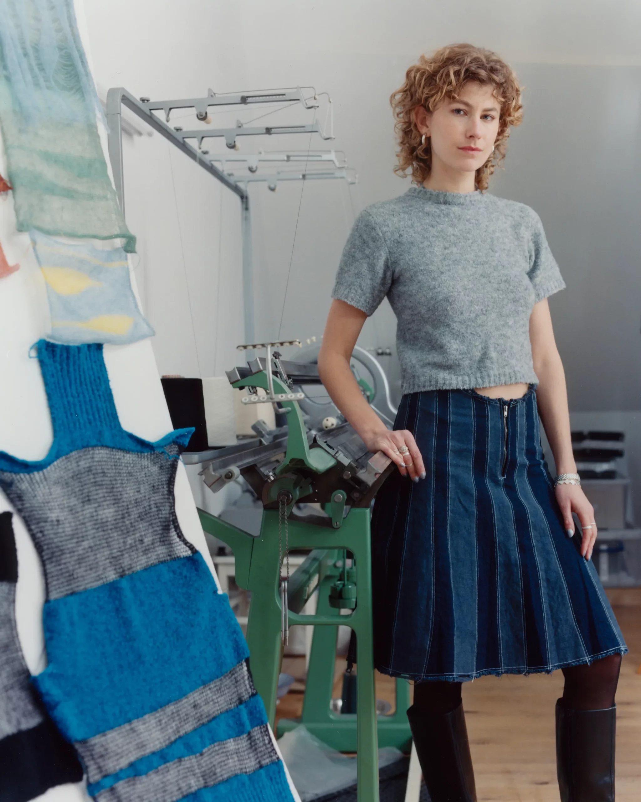 Berlin based Knitwear designer Katharina Dubbick wearing her own designs in her studio in front of a knitting machine. Showing a moodoard of knitting samples. Photographed by Charlotte Helwig.