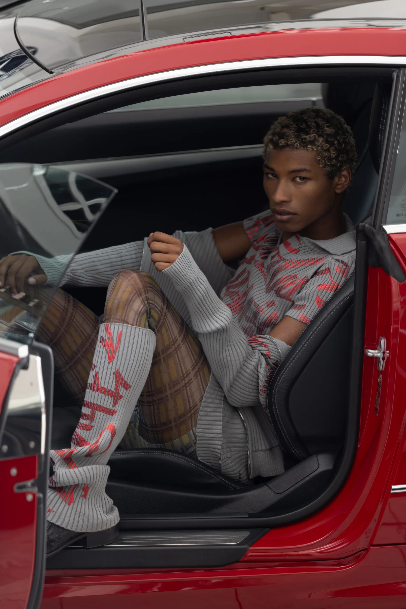 black model with bleached hair wearing Moritz Iden SS25 sitting in a red car. photographed by Tom Fnk.