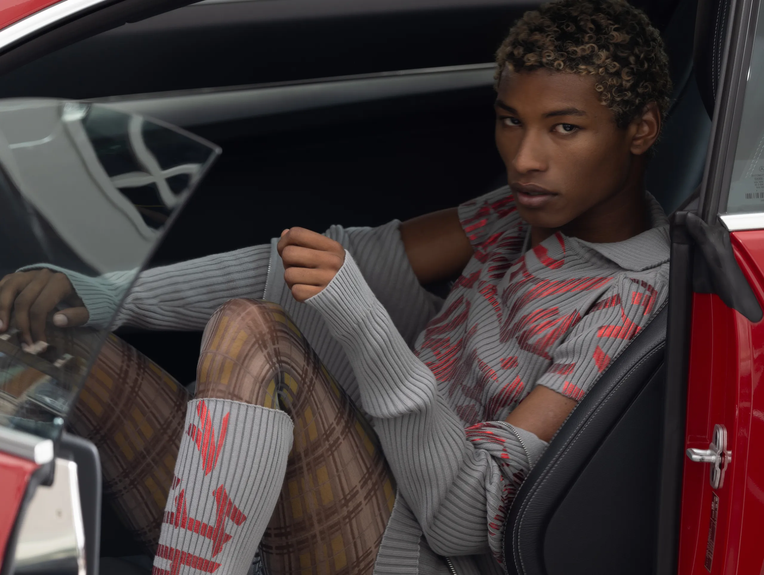 black model with bleached hair wearing Moritz Iden SS25 sitting in a red car. photographed by Tom Fnk.